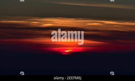 Schöner Sonnenuntergang mit Sonne verschwindet in den dunklen Silhouetten der Vogesen Bergkette mit bunten bewölkten Himmel vom Schauinsland Gipfel aus gesehen. Stockfoto