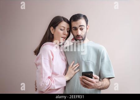 Zwei männliche und weibliche Erwachsene waren überrascht, als sie auf den Telefonbildschirm schauend schockiert waren. Online einkaufen, Spaß haben. Lässiger Kapuzenpullover in Pastellrosa. Leer Stockfoto