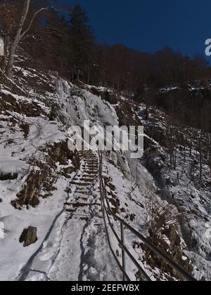 Schneebedeckter Wanderweg mit Stufen und Metallgeländer am steilen Hang der gefrorenen Wasserkaskaden Todtnauer Wasserfälle in der Wintersaison bei Todtnau. Stockfoto