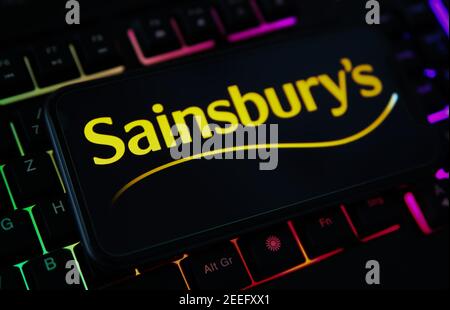 Viersen, Deutschland - Februar 9. 2021: Nahaufnahme des Smartphone-Bildschirms mit Logo-Schriftzug von sainsbury s auf verschwommener Computertastatur Stockfoto