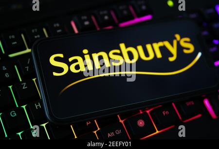 Viersen, Deutschland - Februar 9. 2021: Nahaufnahme des Smartphone-Bildschirms mit Logo-Schriftzug von sainsbury s auf verschwommener Computertastatur Stockfoto