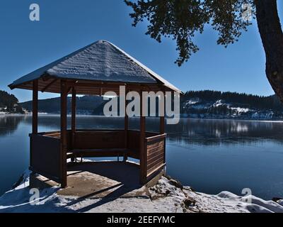 Schneebedeckter Holzpavillon am Ufer des gefrorenen Schluchsees, im Winter ein beliebtes Touristenziel im Schwarzwald. Stockfoto