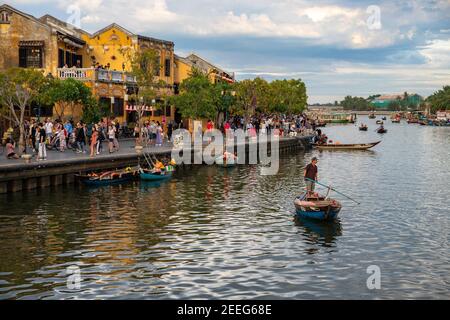 Hoi an, Vietnam - 27 Jul 2019: Historische Stadt am Flussufer mit gelben Gebäuden und Touristen. Traditionelles Holzboot. Hoian Stadtrundfahrt auf dem Fluss. Vietna Stockfoto