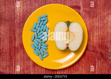 Ausarbeitung einer Diät. Pillen in einem Teller mit einer Apfelhälfte auf einem Holztisch. Gesunde Ernährung, Ernährung, Lifestyle-Konzept. Stockfoto