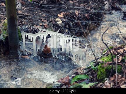 Eiszapfen, die aus Spray wachsen, das auf einen Drahtzaun geworfen wird, der einen Bach durchquert, der durch Buchenwälder in der Nähe von Stroud, Großbritannien, fließt Stockfoto