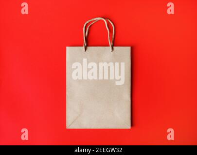 Unbeschriftete braune Papiertüte mit Seilgriffen auf rotem Papierhintergrund. Draufsicht. Flach liegend. Stockfoto