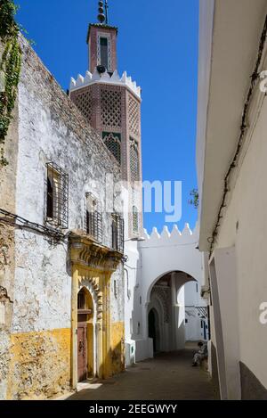 Ein Mann mit gestreifter Djellaba sitzt vor einer kleinen Moschee an der Schwelle eines Hauses in der Medina von Tanger, Marokko. Stockfoto