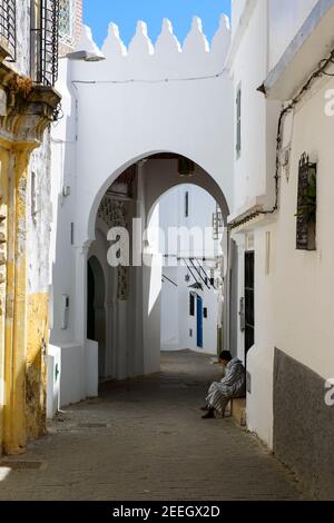 Ein Mann mit gestreifter Djellaba sitzt vor einer kleinen Moschee an der Schwelle eines Hauses in der Medina von Tanger, Marokko. Stockfoto