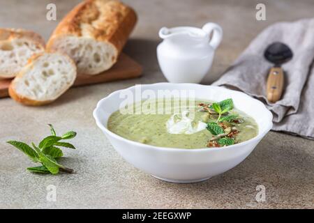 Brokkoli-Sahnesuppe serviert mit Minze, Sahne, Samen und frischem Brot auf Betongrund. Gesunde vegetarische Ernährung Konzept. Selektiver Fokus. Stockfoto