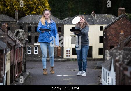 Mutter und Tochter Freiwillige Niki (rechts) und Rachel üben ihre Pfannkuchen werfen in den Straßen von Wimborne Modellstadt und Gärten, während sie am Wimborne Minster virtuellen Pfannkuchen Rennen teilnehmen. Bilddatum: Dienstag, 16. Februar 2021. Stockfoto