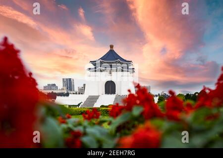 (Selektiver Fokus) Atemberaubender Blick auf die Nationale Chiang Kai-shek Gedenkhalle im Hintergrund und verschwommene rote Blumen im Vordergrund. Stockfoto