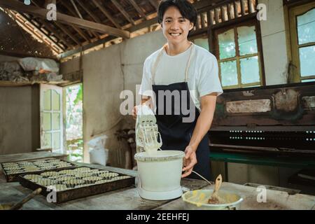 Asian Mann mit einem elektrischen Handmixer bis einige Cookie Teig neben Backblech Kuchen gegen in der Küche Stockfoto
