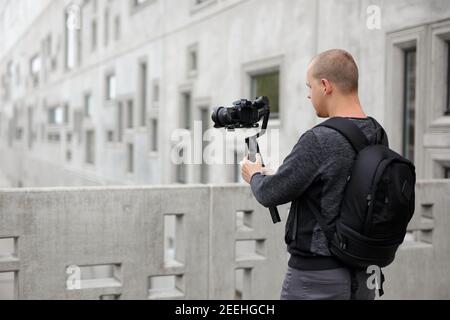 Filmemachen, Hobby und Kreativität Konzept - Rückansicht des professionellen Videografen, der Videos mit moderner dslr-Kamera auf 3-Achsen-Gimbal über concre Stockfoto