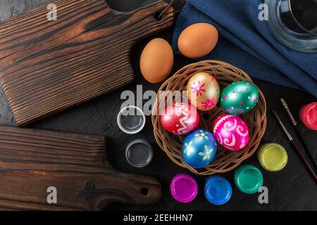Bunte ostern gemalt handgemachte Eier, Farben und Pinsel. Festlicher Osterrahmen aus Eiern, Farben und Pinsel auf schwarzem Hintergrund mit Kopierraum Stockfoto