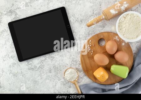Zutaten und Werkzeuge zum Backen und Tablette mit leerem Bildschirm und Platz für Text oder Bild auf weißem Tisch. Rezept, Kochbuch, Kochkurse online tem Stockfoto