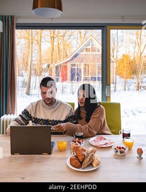 Junges Paar Frühstück mit Laptop.Love, Glück, Menschen und Spaß arbeiten von zu Hause Konzept. Junges Paar mittleren Alters asiatischen und kausischen Mann und Frau arbeiten von zu Hause aus mit Laptop Stockfoto