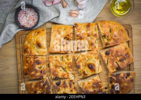 Traditionelle Focaccia von natürlichem Sauerteig Brot mit Rosmarin und Knoblauch. Vollkornfocaccia auf einem hölzernen Hintergrund. Handwerker Stockfoto
