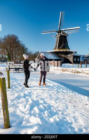 Pelmolen Ter Horst, Rijssen bedeckt in einer verschneiten Landschaft Overijssel Niederlande, historische Windmühle im Winter. Hölzerne alte Windmühle in Holland, Paar Männer und Frau im Schnee zu Fuß Stockfoto