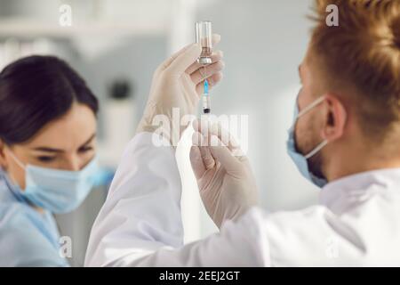 Arzt in Uniform, Maske und Handschuhe Füllen Spritze mit Impfstoff vor der Impfung Stockfoto