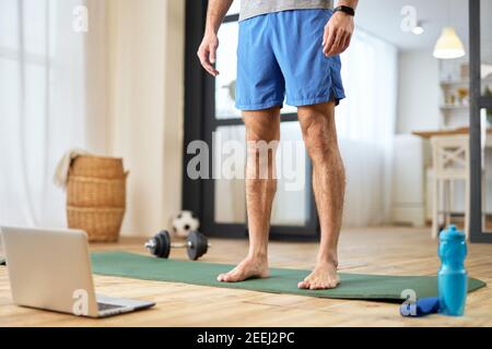 Nahaufnahme eines Barfußherrn, der auf einer Yogamatte steht Vorderseite des modernen Notebooks Stockfoto