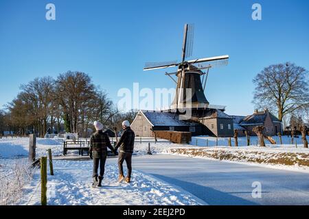 Pelmolen Ter Horst, Rijssen bedeckt in einer verschneiten Landschaft Overijssel Niederlande, historische Windmühle im Winter. Hölzerne alte Windmühle in Holland, Paar Männer und Frau im Schnee zu Fuß Stockfoto