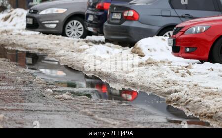 16. Februar 2021, Sachsen-Anhalt, Halle (Saale): Autos parkten zwischen Schneehaufen und spiegeln sich in einer Pfütze. Das beginnende Tauwetter geht bis zum Ende der Woche. Am Wochenende werden zweistellige Temperaturen über Null erwartet. Foto: Jan Woitas/dpa-Zentralbild/dpa Stockfoto