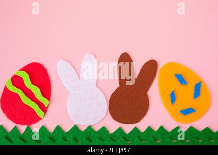 Ausschneiden von Filzanwendungen von Eiern und weißen und braunen Kaninchen auf dem Gras. Rosa Hintergrund. Flach liegend. Osterferien. Speicherplatz kopieren. Stockfoto