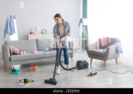 Unglückliche junge Frau saugt chaotisch Wohnung nach der Party, Aufräumen Chaos nach Feiertagsfeier, kopieren Raum Stockfoto