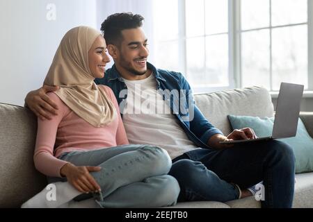 Entspanntes Paar aus dem Nahen Osten sitzt auf der Couch und benutzt einen Laptop Stockfoto