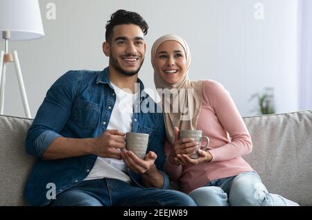 Glückliches Paar aus dem Nahen Osten, das zu Hause auf der Couch sitzt und Tee trinkt Stockfoto