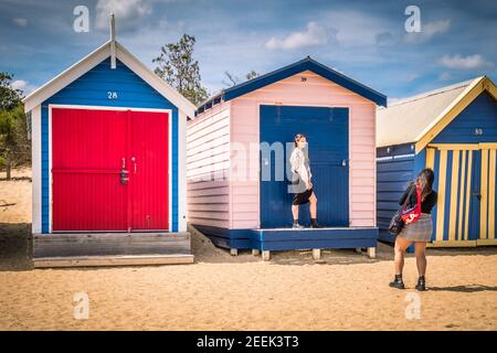 Eine Person fotografiert eine andere vor einem farbenfrohen Strand am Brighton Beach in der Nähe von Melbourne, Australien Stockfoto