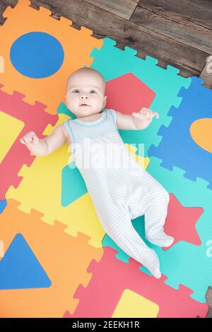 Lachendes Kind auf einer farbigen Gummimatte Puzzle zum Spielen Schaum eva mit geometrischen Figuren Stockfoto