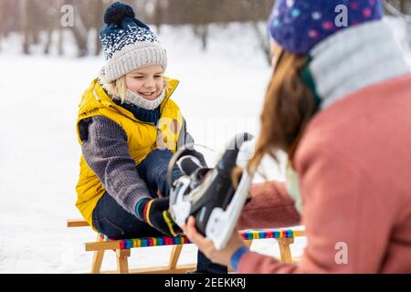 Mutter hilft dem Sohn, seine Schlittschuhe anzuziehen Stockfoto