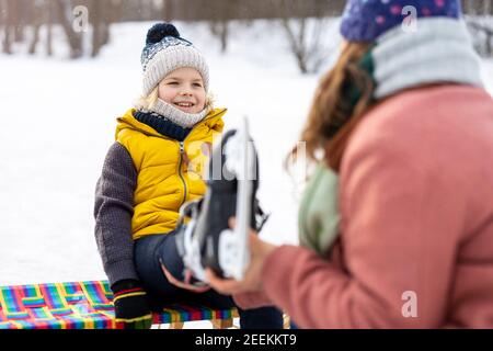 Mutter hilft dem Sohn, seine Schlittschuhe anzuziehen Stockfoto