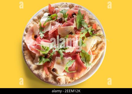 Gourmet-Pizzaprosciutto mit parmaschinken, Scheiben Parmesan und schwarzen Oliven und frischem Rucola-Salat.Flat Lay, Draufsicht auf gelbem Hintergrund Stockfoto