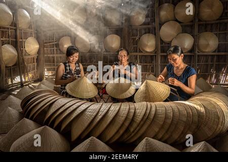 Gruppe von vietnamesischen Kunsthandwerkerinnen Herstellung der traditionellen vietnam Hut in der alten traditionellen Haus in AP Thoi Phuoc Dorf, Hochiminh Stadt, Vietnam Stockfoto