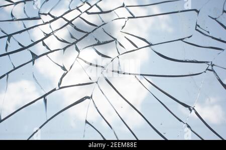 Zerbrochenes Glas mit Rissen auf blauem Himmel Hintergrund. Nahaufnahme der zerbrochenen Glasstruktur Stockfoto