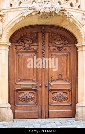 Hellbraune, antike Holztüren mit Schnitzereien und Mustern. Metallgriffe aus Gold. Ein halbkreisförmiges Gewölbe. Eingang zum Haus. Stockfoto