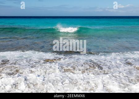 Kristallklares aquamarinfarbenes Meer mit Wellen, die in die Sonne brechen Korallenstrand bei den Sklavenhäusern auf der Karibikinsel Von Bonaire Stockfoto