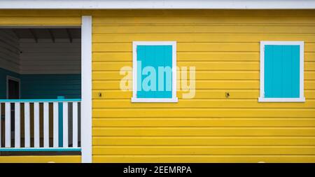 Sanft beleuchtetes, gelb gestrichenes Holzgebäude mit 2 geschlossenen, weiß gerahmten, blau gestrichenen Fensterläden und einer geschlossenen Veranda mit Platz für Kopien Stockfoto