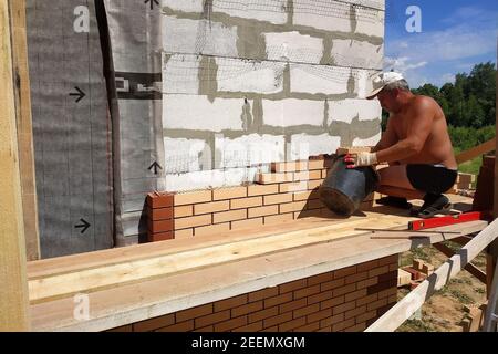 Der Meister stellt das Mauerwerk aus dem vorderen Ziegel, die Erwärmung des Hauses draußen, die Bauarbeiten im Sommer.neu Stockfoto
