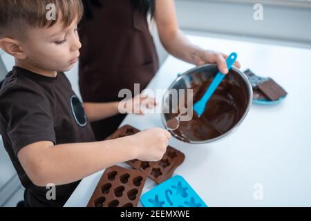 Glückliche Mutter und Kind Herstellung Schokolade Bonbons oder Süßigkeiten an Startseite Moderne Küche Stockfoto