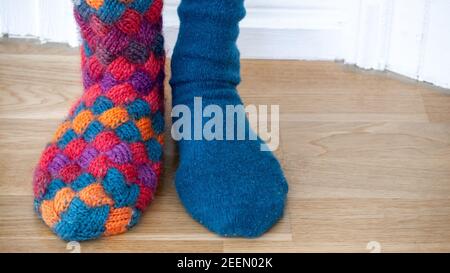 Eine Person trägt ein Paar von verschiedenen bunten gestrickten Hand gemacht warme Socken, auf dem Boden stehend. Nahaufnahme. Stockfoto