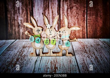 Drei hölzerne Osterhasen mit Dekoration und dem Text Ostern auf Eiern geschrieben. Stockfoto