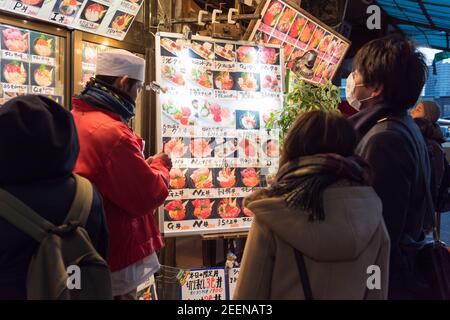 Tokio, Japan - Jan 22 2016: Touristen, die sich die Angebote eines Restaurants mit Meeresnahrung auf dem berühmten Tsukiji-Markt in Tokio, Japan, angeschaut haben. Stockfoto