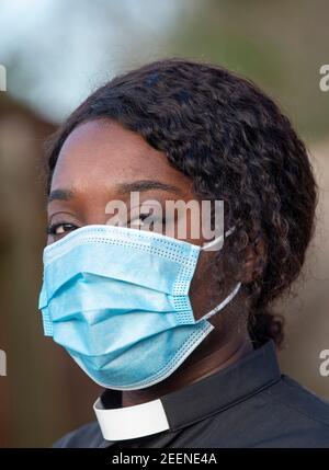 England, Großbritannien, Dezember 2020. Ein schwarzer Minister, der während des Coronavirus-Ausbruchs eine medizinische Schutzmaske und ein weißes Halsband trägt Stockfoto