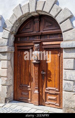 Hellbraune, antike Holztüren mit Schnitzereien und Mustern. Metallgriffe aus Gold. Ein halbkreisförmiges Gewölbe. Eingang zum Haus. Stockfoto