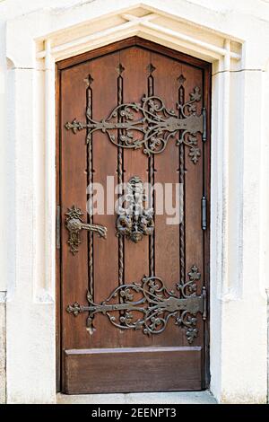 Hellbraune, antike Holztüren mit Schnitzereien und Mustern. Metallgriffe aus Gold. Ein halbkreisförmiges Gewölbe. Eingang zum Haus. Stockfoto