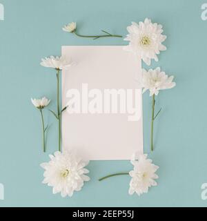 Kreatives Layout mit weißen Gänseblümchen-Blumen und Papier Karte Notiz auf dem weichen grünen Hintergrund gemacht. Minimal Frühling oder Sommer flach lag. Stockfoto