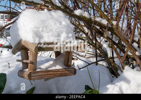 Ein Vogelfutterhäuschen aus Holz, das mit Schnee bedeckt ist. Hier werden die Vögel im Winter gefüttert. Stockfoto